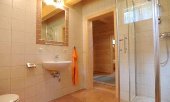 A modern bathroom with a shower and a sink. An orange towel is hanging on the wall.