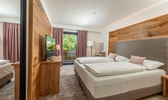 A modern hotel room with two beds and wooden elements. Large windows let in daylight and offer a view of nature.