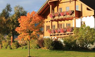 A beautiful wooden house with blooming balcony boxes and a bright orange tree in the foreground. The surroundings are green and inviting, perfect for a peaceful day outdoors.