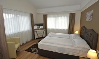 A modern bedroom with a large double bed and bright curtains. A cozy seating area and a dresser complement the furnishings.