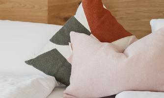 A cozy bed with colorful pillows and a wooden frame. The walls are painted in a soft green.