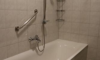 A bathroom with a bathtub and a shower. The walls are tiled and there is a shelf for toiletries.