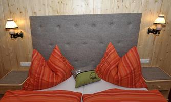 A cozy bedroom with a large, padded headboard and bright orange pillows. Stylish wall lamps are hanging on the walls.