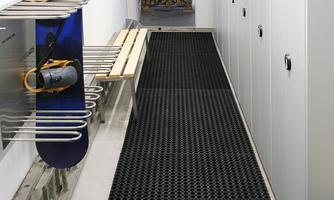 A spacious hallway with lockers and storage for snowboards. The floor is equipped with a black mat that ensures slip resistance.