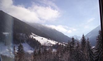 A picturesque winter landscape with snow-covered mountains and dark fir trees. The sky is clear with some clouds.