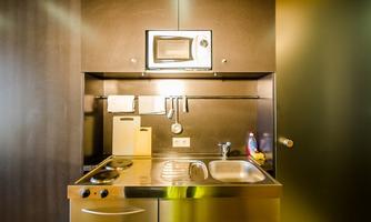 A modern kitchenette with a stainless steel surface. It features a stove, a sink, and a microwave.