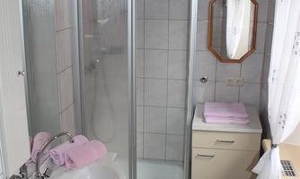 A small bathroom with a modern glass shower and a sink. There are pink towels and plenty of daylight from a window.