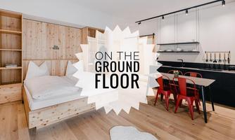 A modern apartment with wooden shelves and a large bed. A dining group with red chairs complements the open kitchen.