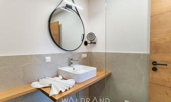 A modern bathroom with a round mirror and an elegant wooden vanity top. The walls are painted in neutral tones, creating a relaxed atmosphere.