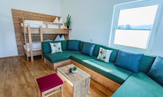 A modern room with a cozy sofa bed and a wooden loft bed. Bright walls and large windows create an inviting atmosphere.