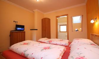 A bright bedroom with two beds and colorful bedding. There is a television on the wall and a large mirror.
