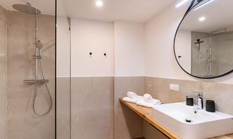 A modern bathroom with a glass shower and a sink made of white ceramic. The walls are in neutral tones and there is a large mirror.