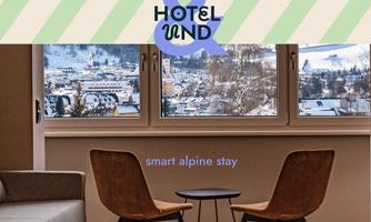 A modern furnished room with two armchairs and a table, offering a view of a picturesque alpine landscape. Large windows let in plenty of light and provide an inviting atmosphere.