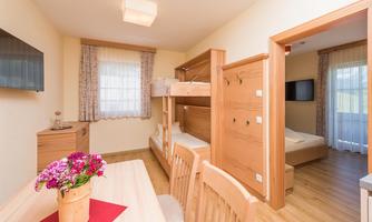 A cozy living space with a bunk bed, a table, and chairs. Bright walls and windows create a friendly atmosphere.