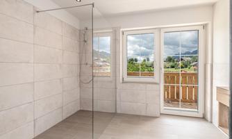 A modern bathroom with a large glass shower. The windows offer a view of the green landscape outside.