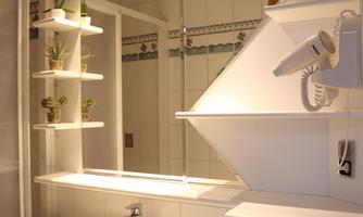 A modern bathroom with a bright sink and a large mirror. Shelves with plants add a fresh touch.