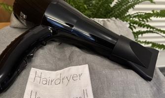 A hair dryer lies on a gray cloth. Next to it is a label with the inscription "Hair Dryer. Use only in the rooms!!".