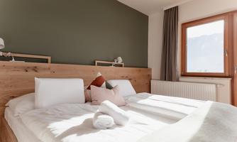 An inviting bedroom with a large bed and bright, modern furniture. The room has a warm atmosphere and a view of the mountains through the window.