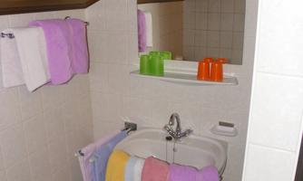 A bathroom with a sloped ceiling and a sink. Colorful towels hang over the sink and there are toiletries on the shelf.