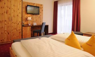 A cozy hotel room with wooden ceilings and furniture. It features a double bed, a desk, and a television.