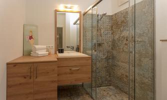 A modern bathroom with a glass shower and a wooden cabinet. Fresh towels are on the sink.