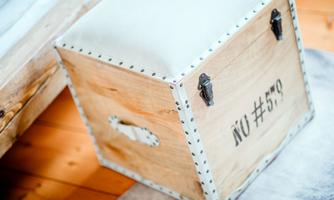 A stylish wooden box with a padded lid. It features decorative metal fittings and a labeled side.