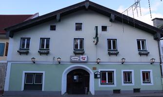 A traditional building with a green facade and white windows. It is located in a city and has inviting lights on the facade.