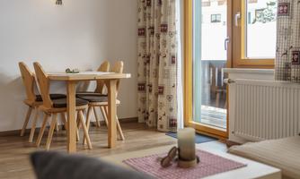 A cozy dining area with a wooden table and chairs. Large windows offer views outside and plenty of daylight.