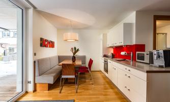 A modern kitchen with an adjoining dining area. The room is bright and friendly, with red accents and stylish furniture.