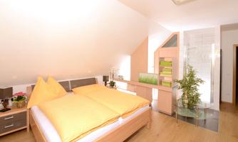 A modern bedroom with a large bed and yellow pillows. The room is bright and has an elegant decor with a desk and plants.