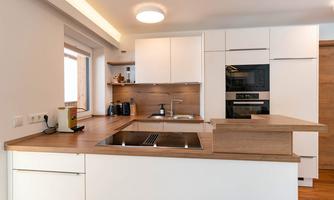Modern kitchen with white cabinets and wooden surfaces. Well equipped with appliances and a large window for natural light.