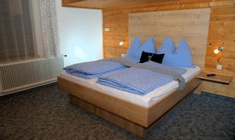 A modern bedroom with a wooden panel and a large bed. The pillows are in a checked design and the walls are made of wood.