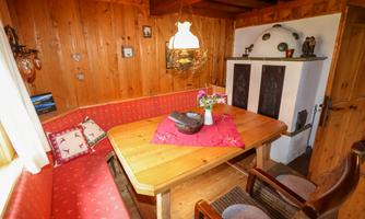 A cozy dining area with a wooden table and a red bench. The wall is made of wood, and there is a lamp as well as decorative elements in the background.