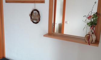 A bright hallway with a wooden bench and a large mirror. On the wall hangs a coat rack and a small flower vase.