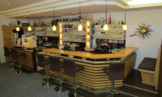 A modern bar with wooden details and cozy stools. Behind the counter, various drinks and glasses are displayed.