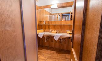 A cozy bathroom with wooden walls and a sink. Towels are neatly placed on the shelf.