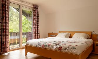 A modern bedroom with a comfortable bed and colorful curtains. Large windows offer a view of nature outside.