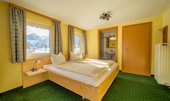 A cozy bedroom with two beds and yellow walls. Large windows offer a view of the mountains.