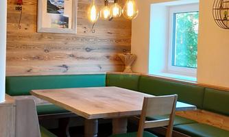A cozy room with a wooden bench and a wooden table. The walls are clad with wood, and stylish lamps hang from the ceiling.