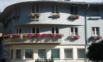 A modern building with a curved facade and blue walls. The balconies are decorated with colorful flowers.