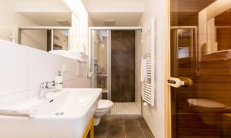 A modern bathroom with a washbasin, a shower, and a toilet. The walls are bright and the furnishings are simple and functional.