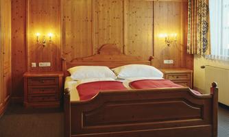 A cozy bedroom with a wooden bed and red bedding. Warm wooden walls and a pleasant atmosphere.