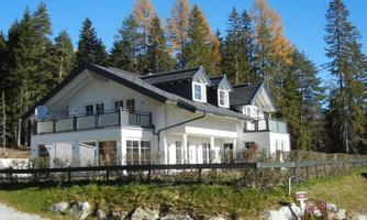 A modern house in a quiet, wooded setting. It has large windows and a balcony to enjoy the view.
