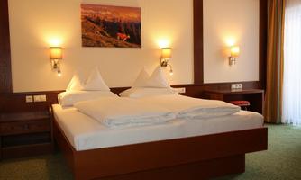 A cozy hotel room with a double bed and two small pillows. There is a picture hanging on the wall, and the room has windows with natural light.