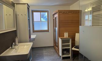 A modern bathroom with a sink, a wooden sauna, and ample daylight. Bright walls and a clear design create an inviting atmosphere.