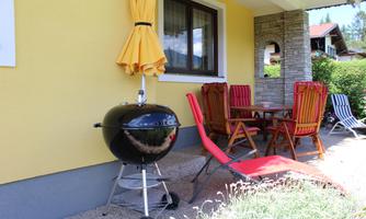 A cozy outdoor area with a charcoal grill and a dining table. Red and colorful chairs provide space for relaxation.