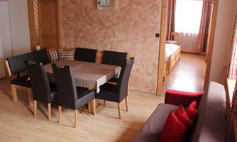 A cozy living space with a dining area and a sofa. The wooden floor and warm colors create an inviting atmosphere.