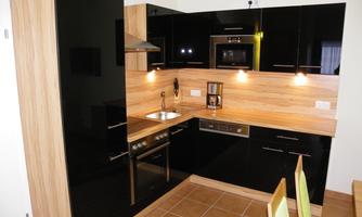 A modern kitchen with black high-gloss fronts and wooden shelves. The equipment includes a stove, a microwave, and a coffee maker.