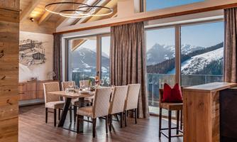 An elegant dining room with a table and chairs. Large windows offer a view of the mountains and the surrounding nature.