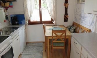 A bright, small kitchen with a table and chairs. Light streams in through the window, and there are kitchen utensils on the table.